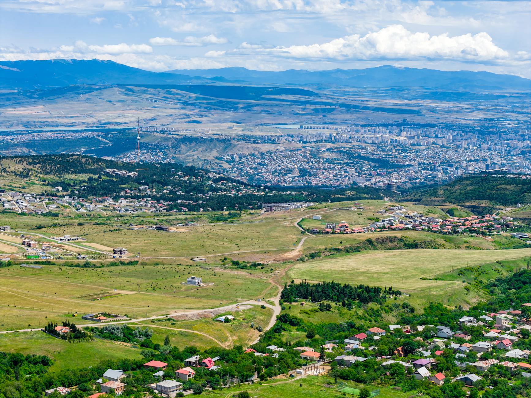 A stunning aerial view showcasing Tbilisi's sprawling cityscape and surrounding countryside on a clear day.