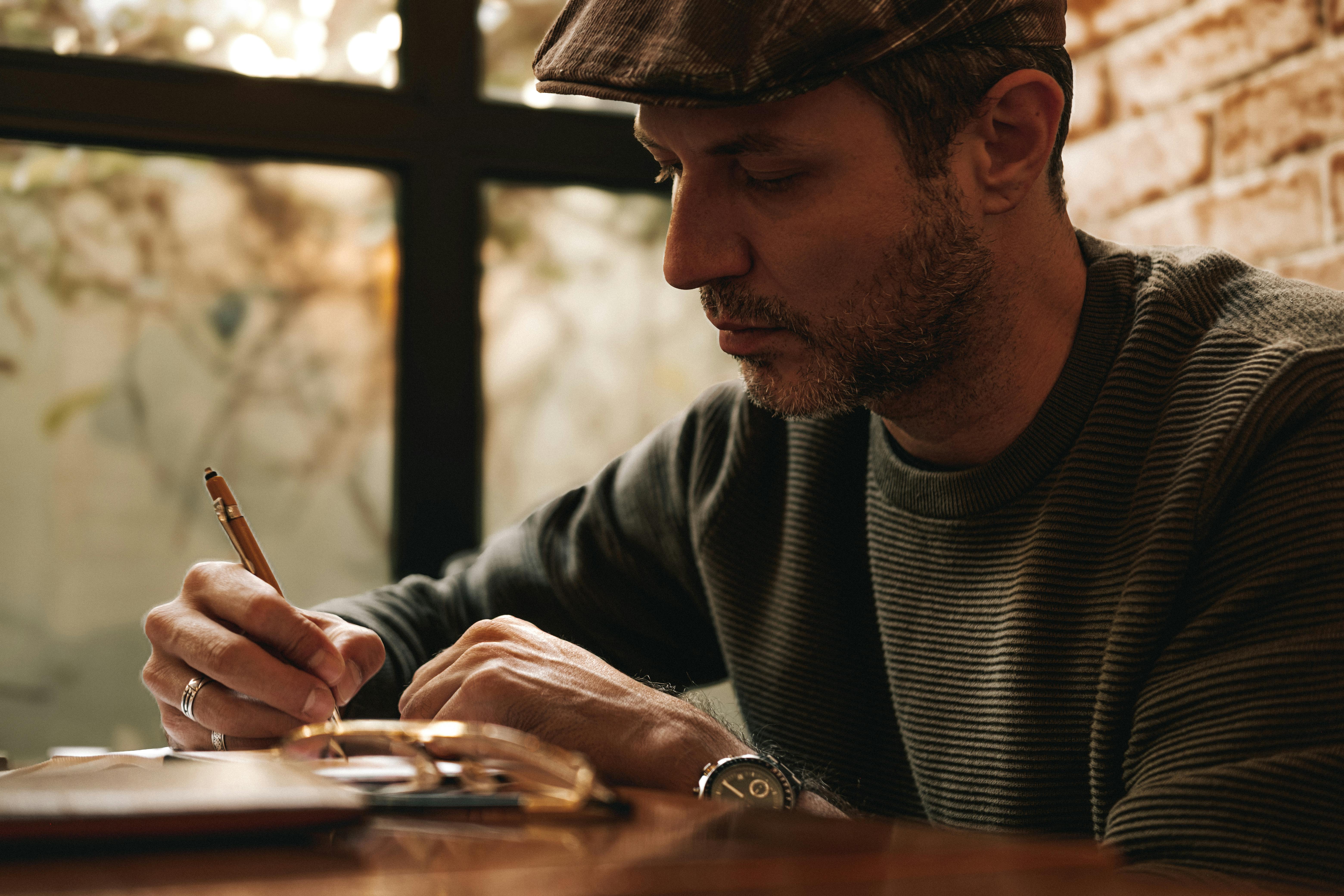 Thoughtful man writing in a notebook with a pen in a warm, cozy indoor environment.