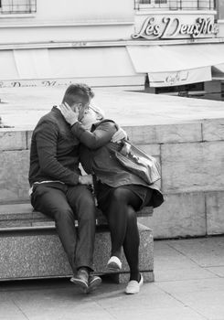 Couple sharing a tender kiss in front of a famous Parisian cafe, Les Deux Magots.