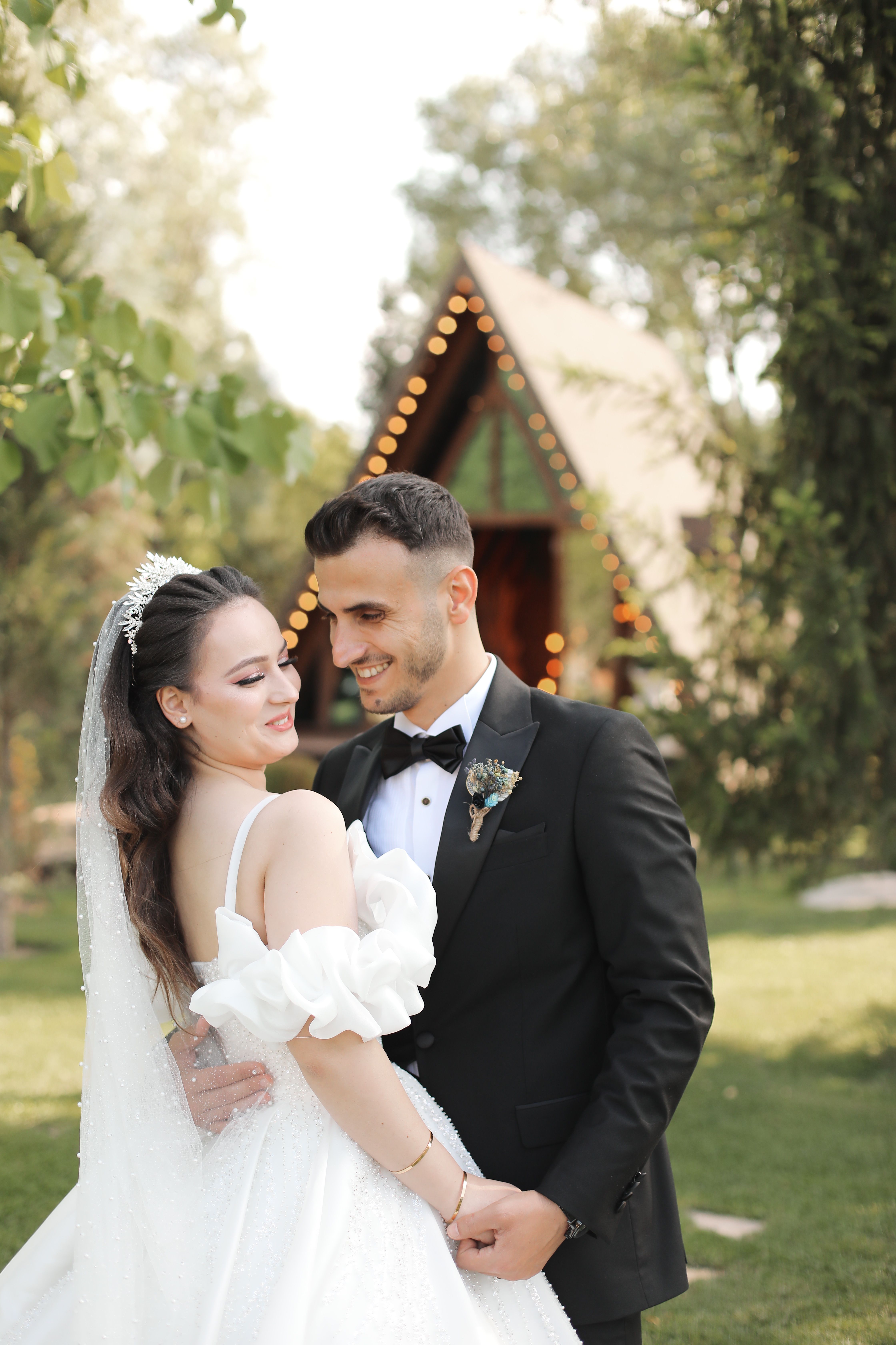 Beautiful couple embracing outdoors in wedding attire with greenery backdrop.