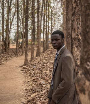 A man in a suit stands in an autumnal forest, creating a moody portrait.