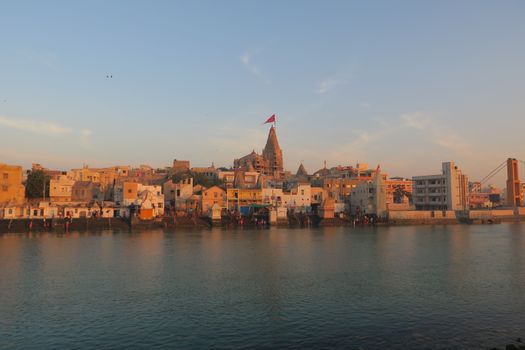 View of the historic Dwarka city and temple by the river at sunset, capturing its architectural beauty.