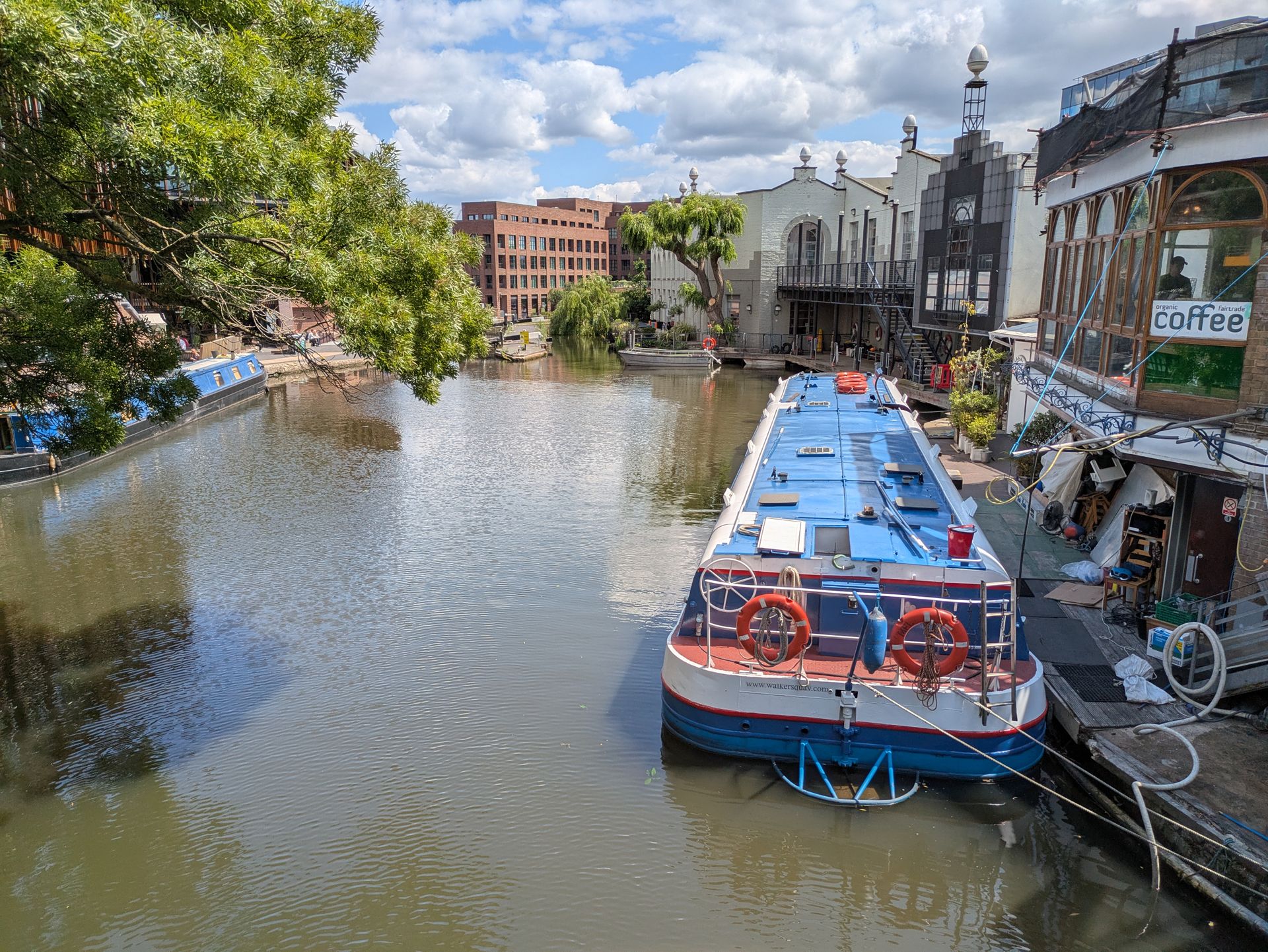 Charming view of canal boats on Regent's Canal in London on a sunny day, with trees and historic buildings.