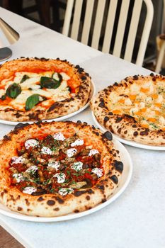 Three gourmet pizzas with toppings sitting on a white marble table ready to eat.