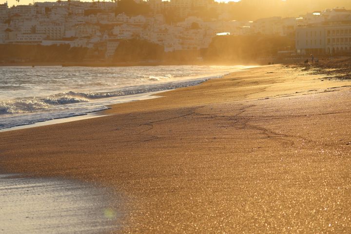 Sunset view of a golden beach with sparkling sand and soft ocean waves.