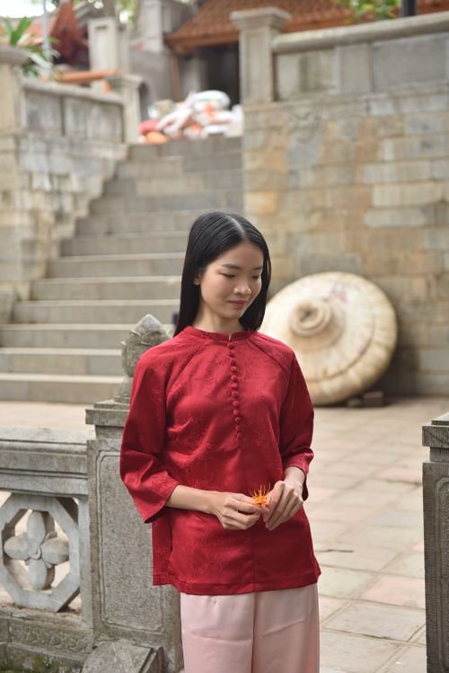 Free Young woman in red traditional dress beside stone staircase holding a flower. Stock Photo