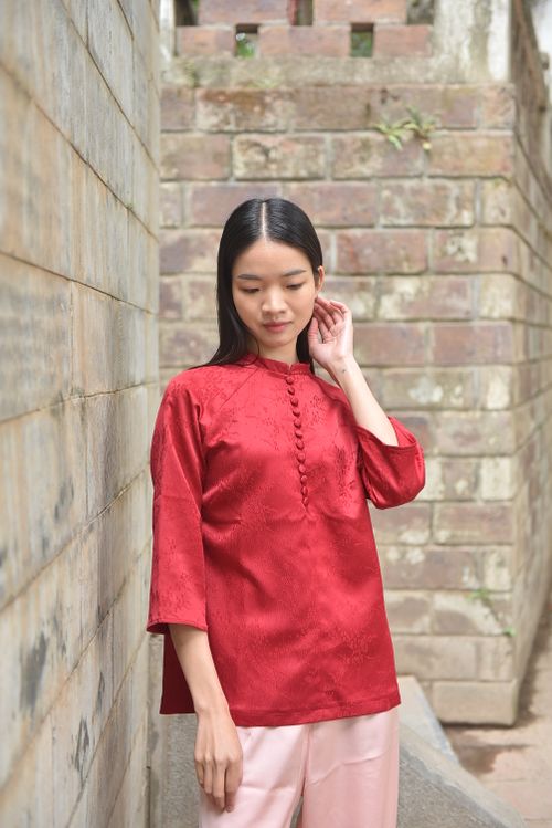 Free Young woman wearing a red qipao standing by a brick wall, looking thoughtful. Stock Photo
