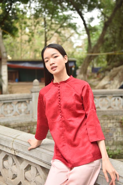 Free Young woman in vibrant red traditional clothing posing outdoors near stone railing. Stock Photo