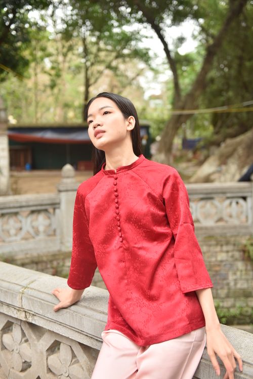 Free Woman in traditional red attire leaning on a stone railing in a serene outdoor setting. Stock Photo