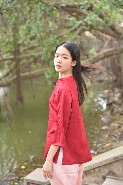 Free A woman in a red dress stands by a calm pond surrounded by lush greenery. Stock Photo
