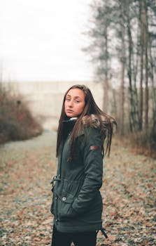 一位穿着温暖夹克的年轻女子，自信地站在秋季森林中摆出姿势