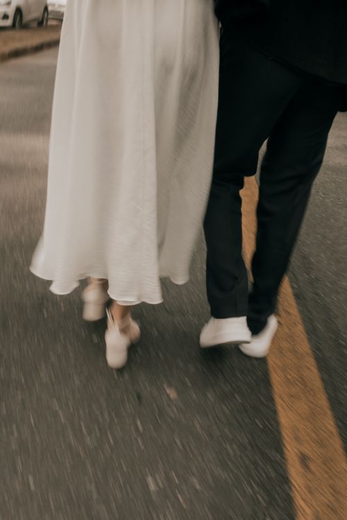 Free A couple in wedding attire walking closely on a street, capturing a romantic moment. Stock Photo