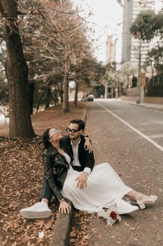 Happy couple sitting on a leaf-strewn road during autumn, capturing a romantic and candid moment.