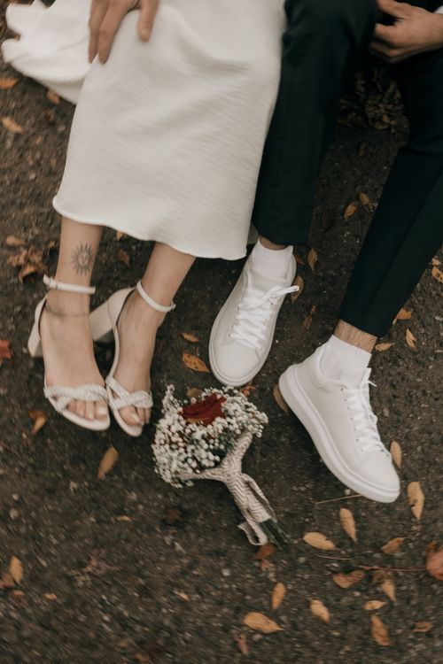 Free Couple's legs in sneakers and heels on autumn leaves with bouquet. Stock Photo