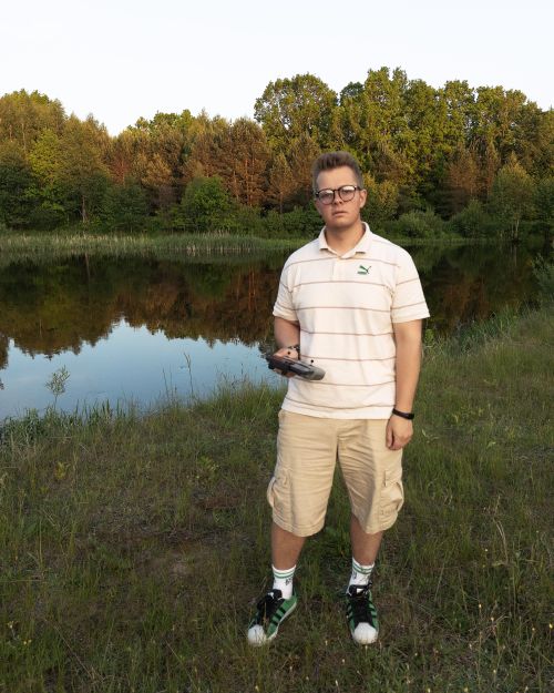Free A young man holding a drone controller stands by a serene pond in Belarus, surrounded by lush greenery. Stock Photo