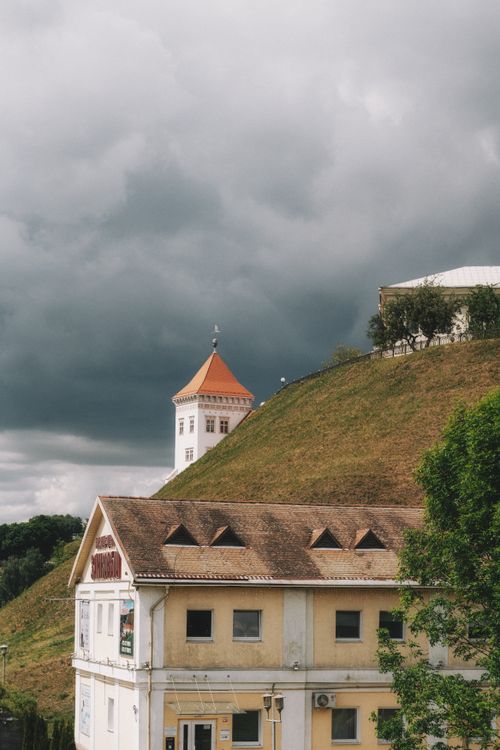 Free A historic white tower with an orange roof stands against a dramatic cloudy backdrop. Stock Photo