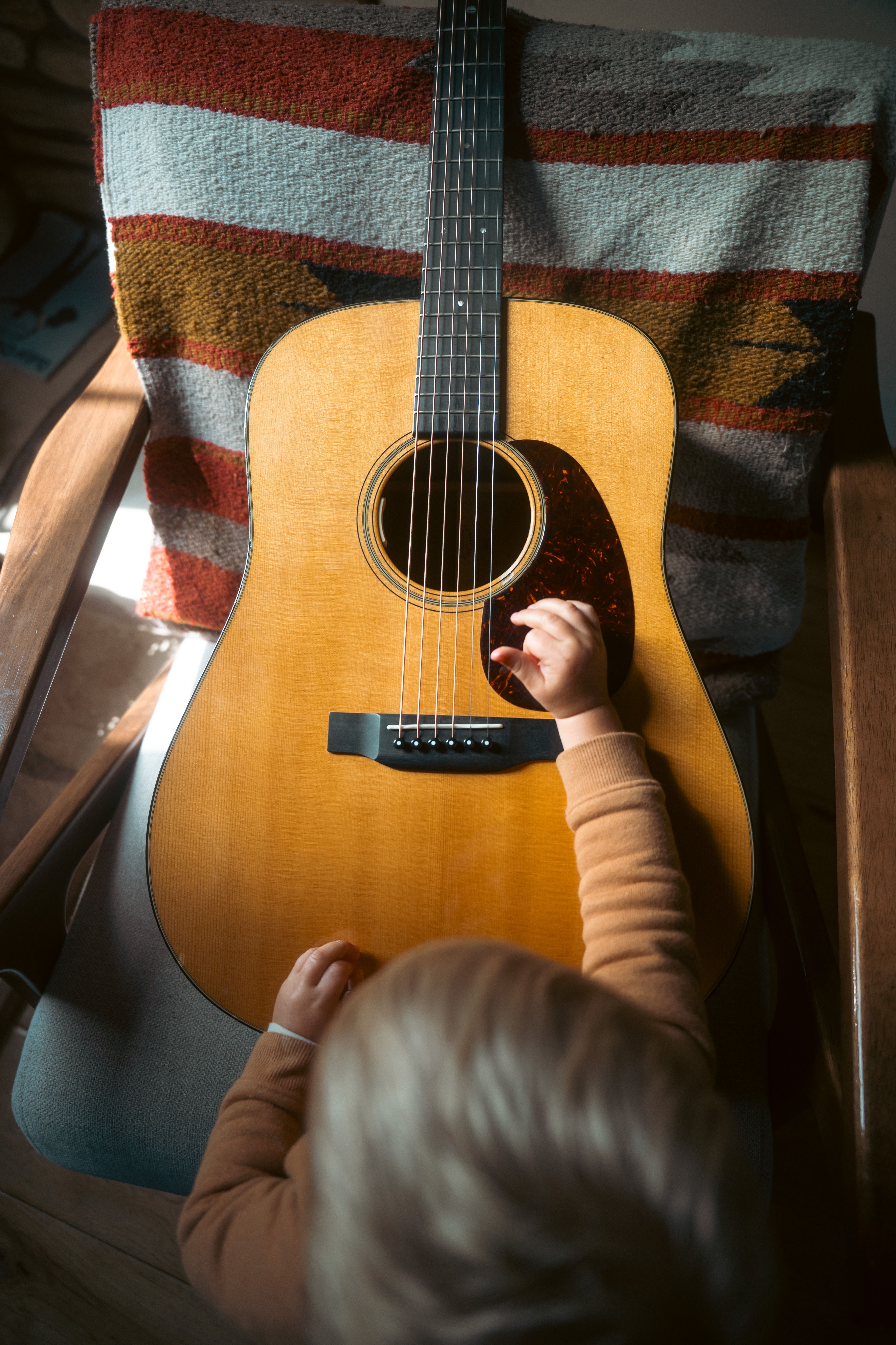 A child reaching for an acoustic guitar on a cozy chair indoors.