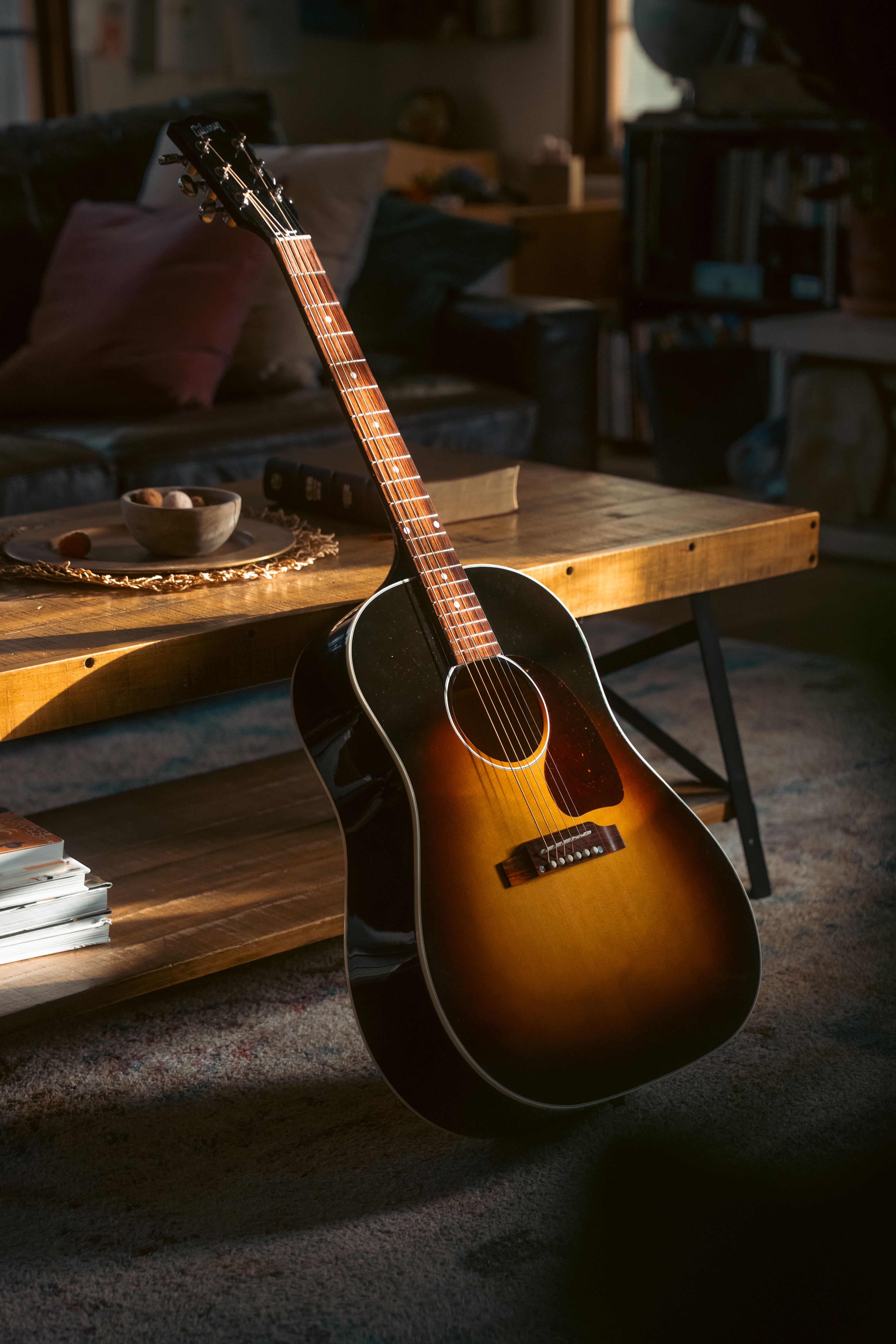 Warmly lit acoustic guitar leaning against a rustic coffee table in a cozy living room setting.
