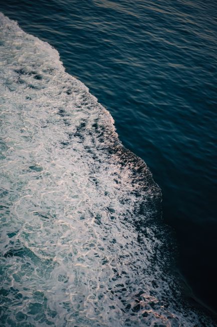 Stunning aerial view of ocean waves crashing against the shore at sunset, creating a serene atmosphere.