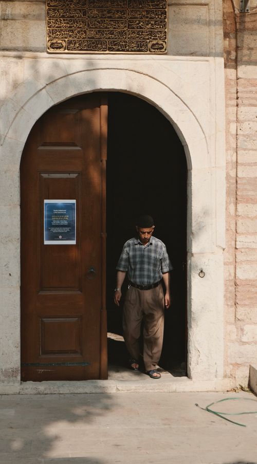 Free Man in casual attire exits historic building through arched doorway, casting a shadow. Stock Photo