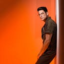 一位穿着绿色服装、戴着眼镜的时尚年轻人在充满活力的橙色背景下摆着姿势