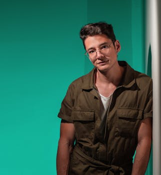 一位戴着眼镜、身穿时尚连身裤的男模特肖像，背景为绿色