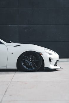 Close-up of a white sports car's front side against a modern black wall.