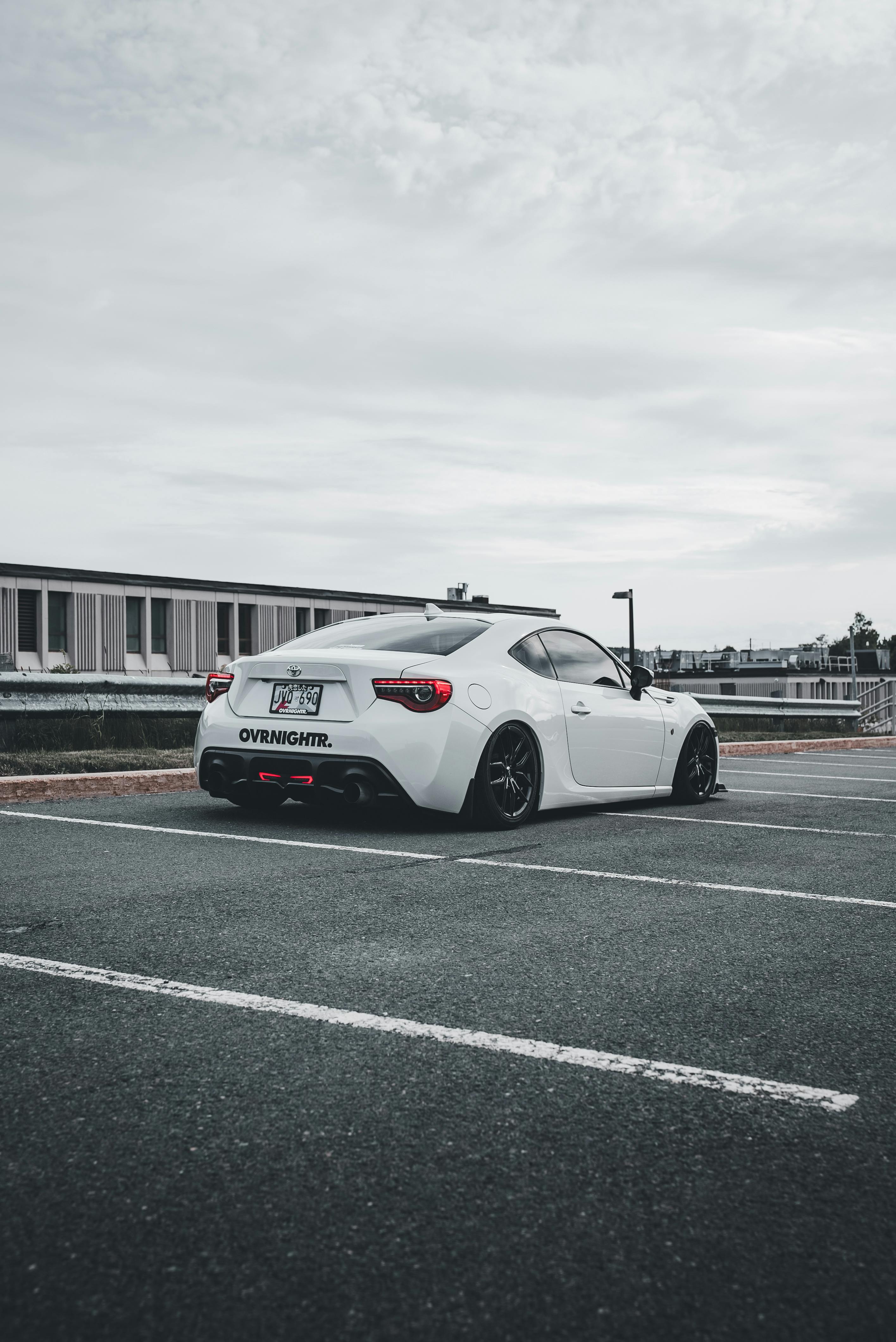 White sports car parked in an urban parking lot on a cloudy day.