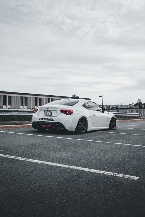 Free White sports car parked in an urban parking lot on a cloudy day. Stock Photo