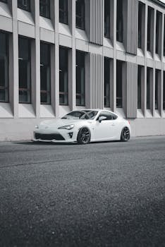 Modern white sports car parked beside an urban building on a quiet street.
