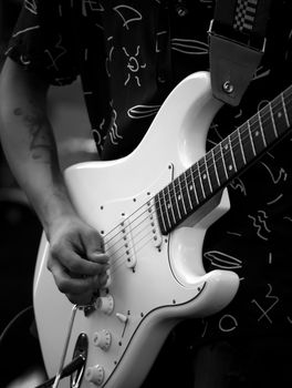 Black and white photo of a guitarist's hands playing a white electric guitar.