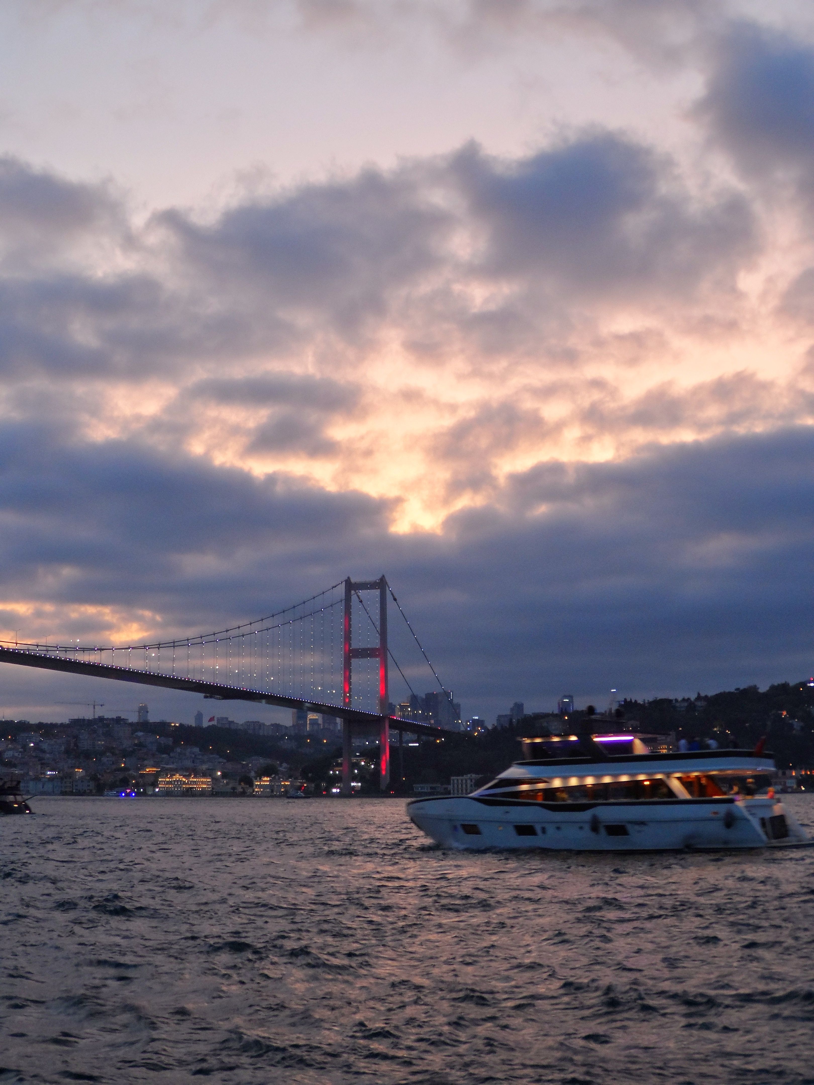 Free Boat cruising on the Bosphorus at sunset with Istanbul's Bosphorus Bridge illuminated. Stock Photo