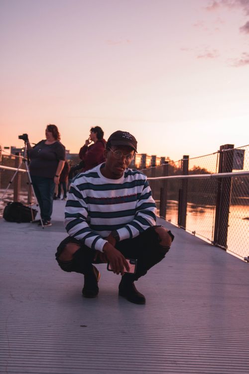 Free A male model in casual wear posing on a pier during sunset with photographers in the background. Stock Photo