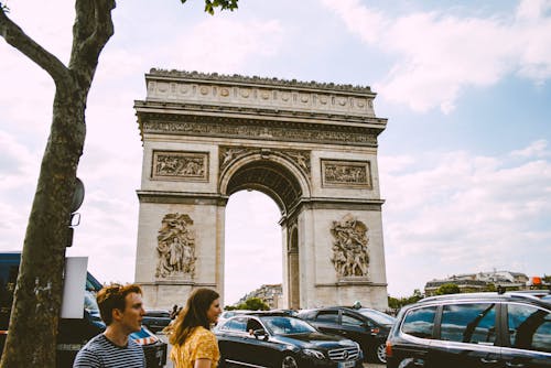 Two Man and Woman Near Cars and White Concrete Arc Gate during Dayrtime