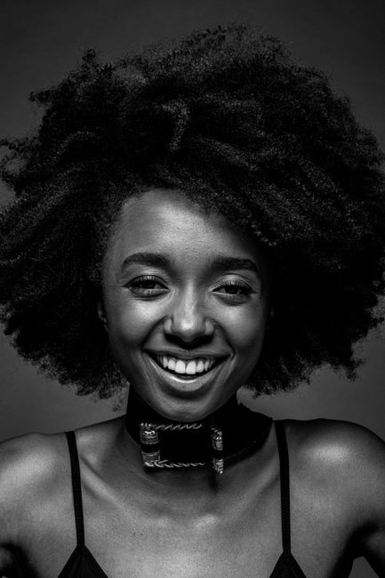 Captivating black and white portrait of a smiling woman with curly afro hair in a studio setting.