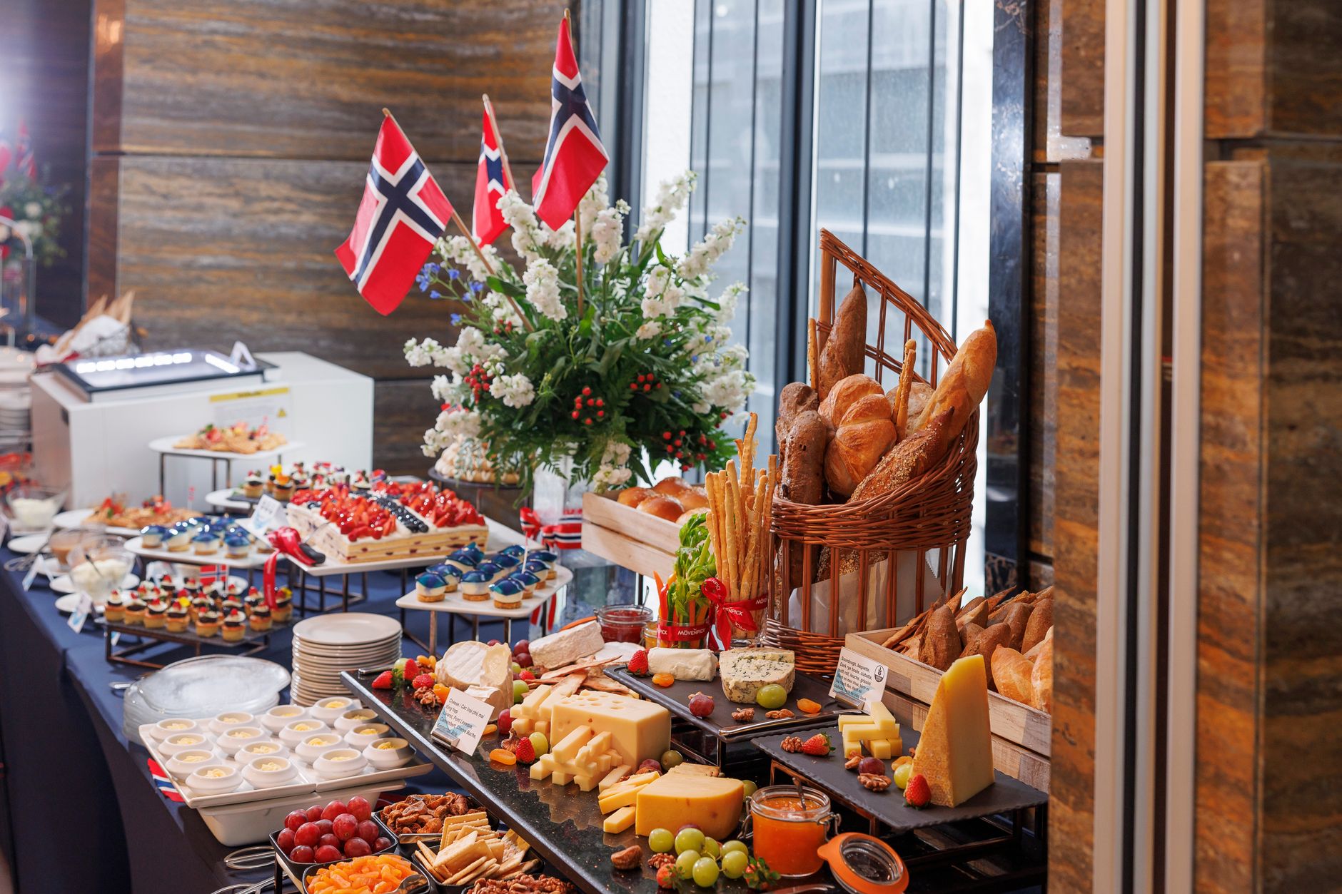 A lavish buffet spread featuring a variety of breads, cheeses, and Norwegian flags indoors.