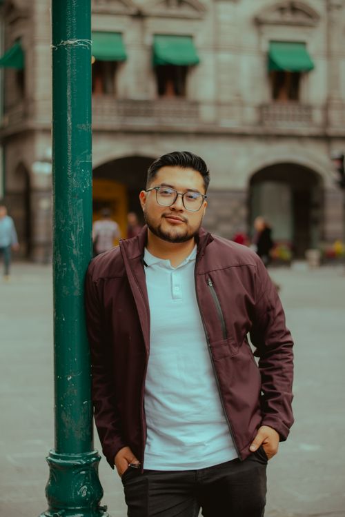 Free Young man with glasses in a burgundy jacket posing casually in a city environment. Stock Photo