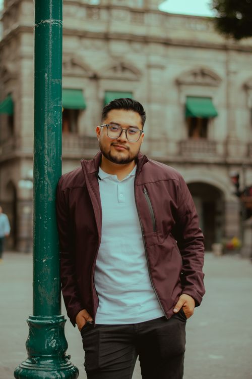 Free Casual portrait of a man leaning on a pole in an urban environment, featuring classic architecture. Stock Photo