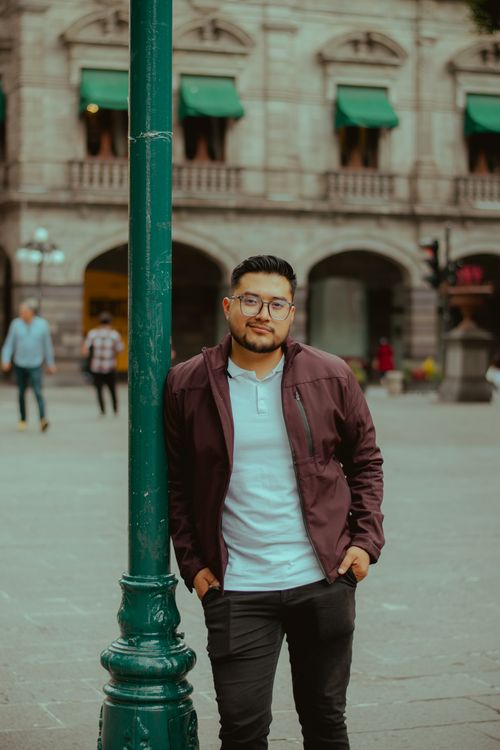 Free Young man in casual attire leaning against a lamppost in an urban setting, showcasing fashion and street vibes. Stock Photo