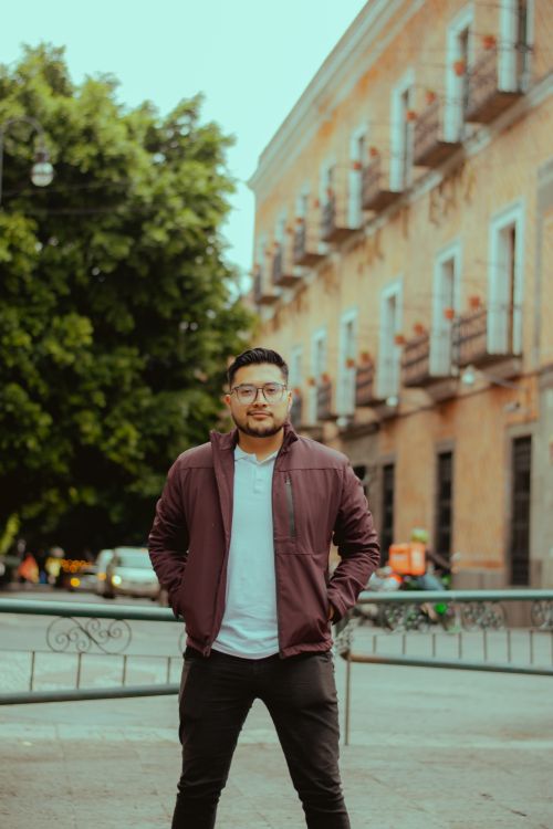 Free Young man in casual attire stands confidently on a historic city street, showcasing urban lifestyle. Stock Photo