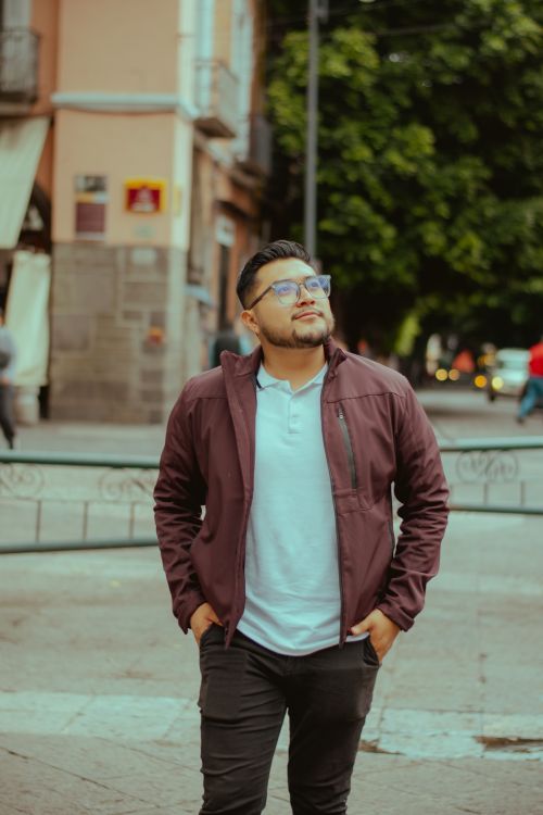 Free A stylish young man in a city street wearing glasses and a jacket, looking thoughtful. Stock Photo