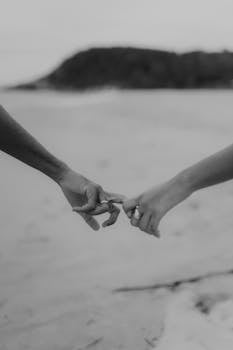 Black and white photo of two people holding hands on a serene beach.