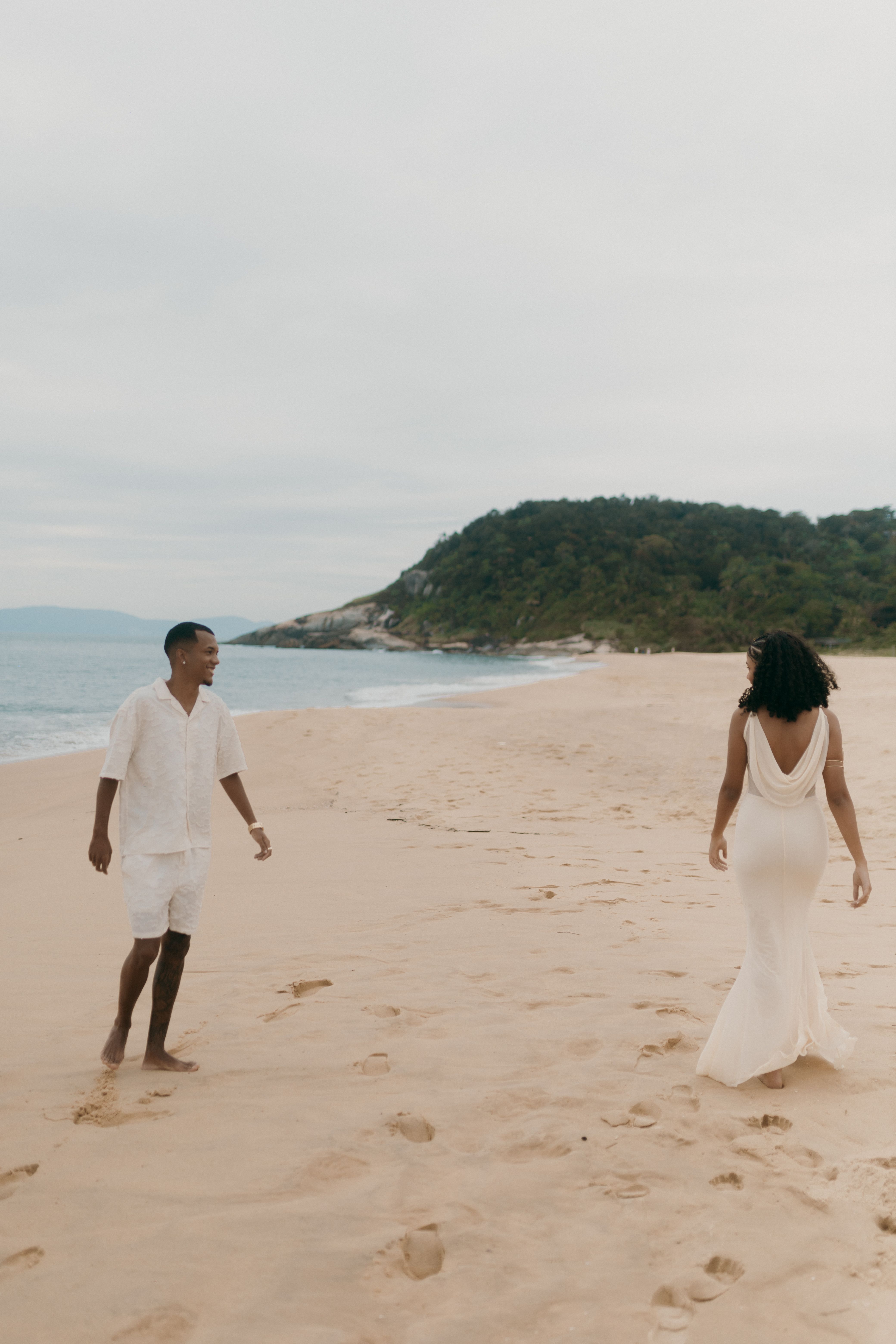 Couple strolling along a wide sandy beach with a lush green headland behind them