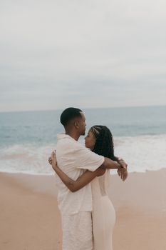 A loving couple embraces on a peaceful beach with gentle waves in the background.