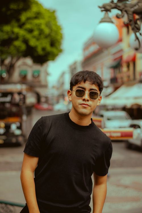 Free Confident young man wearing sunglasses walking in a vibrant city street. Stock Photo