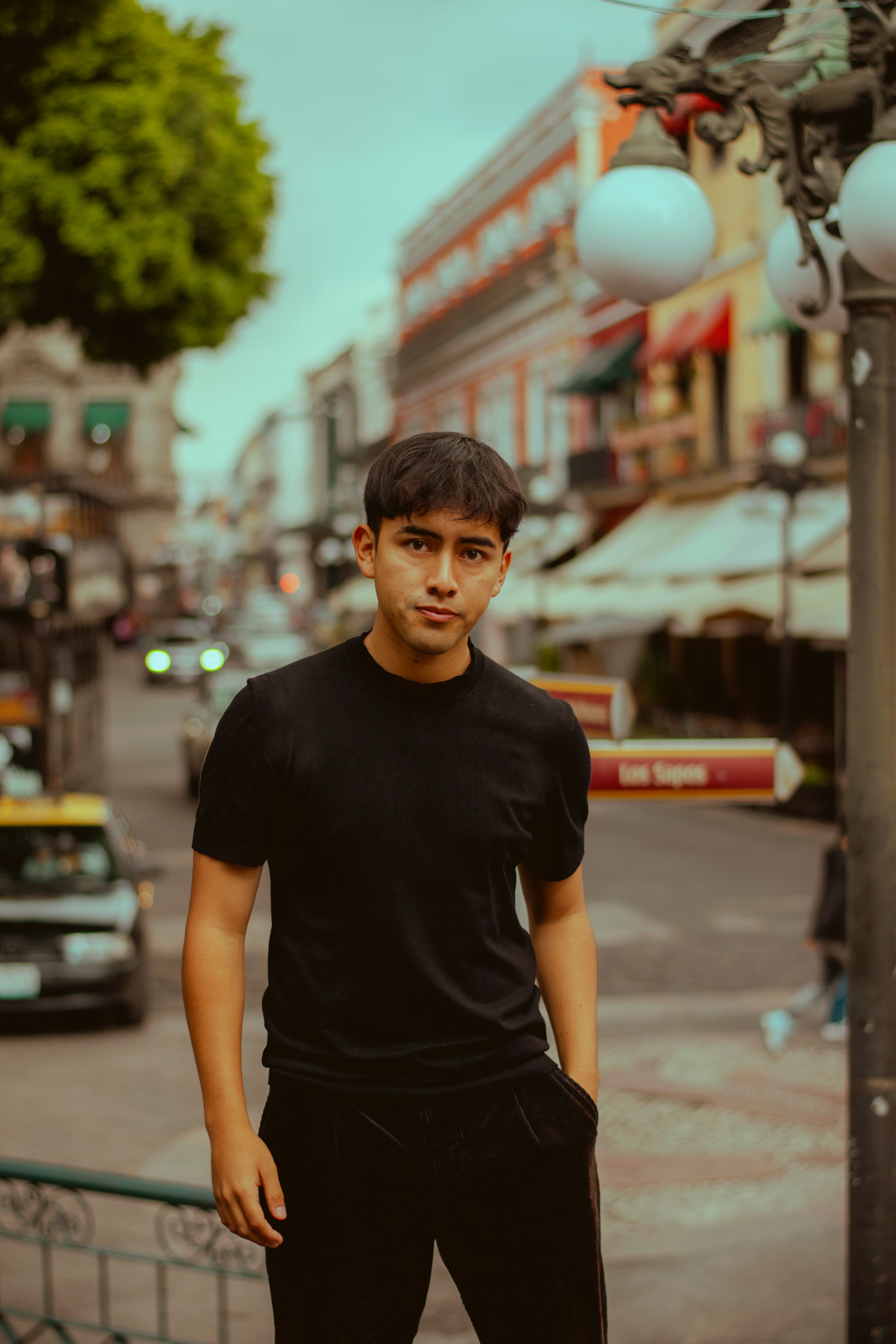 Portrait of a young man in a black shirt standing confidently on a lively city street.