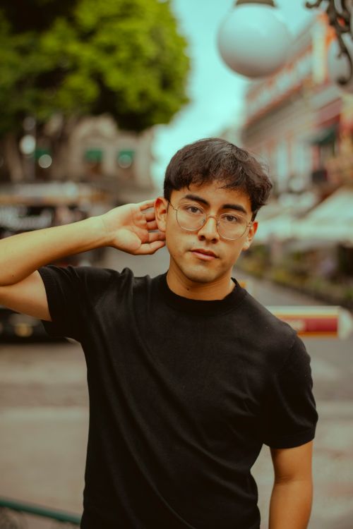 Free A young adult man poses outdoors in a relaxed urban environment wearing glasses. Stock Photo