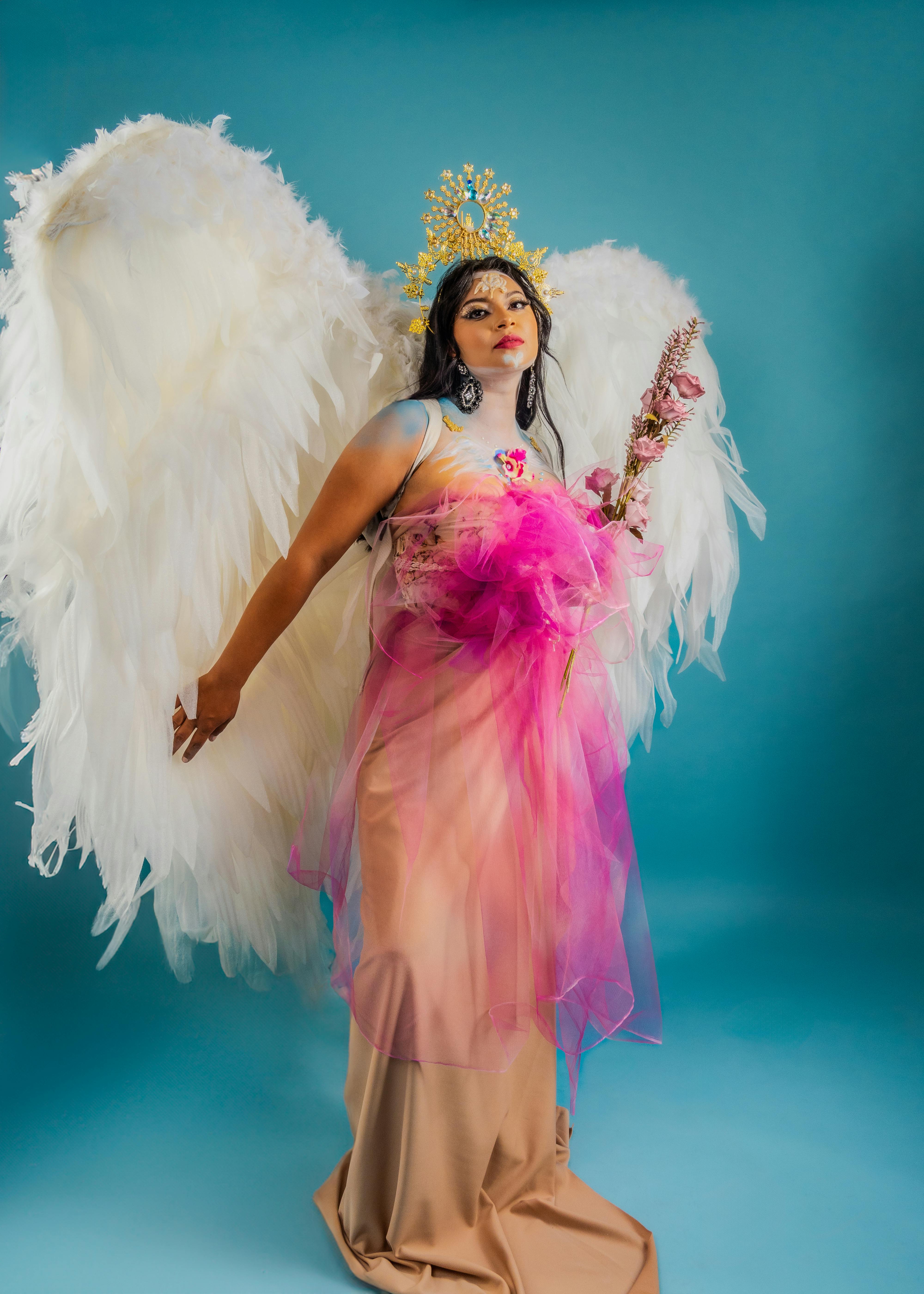 Angel-inspired woman in a vivid gown and wings exudes artistic elegance against a vibrant backdrop.