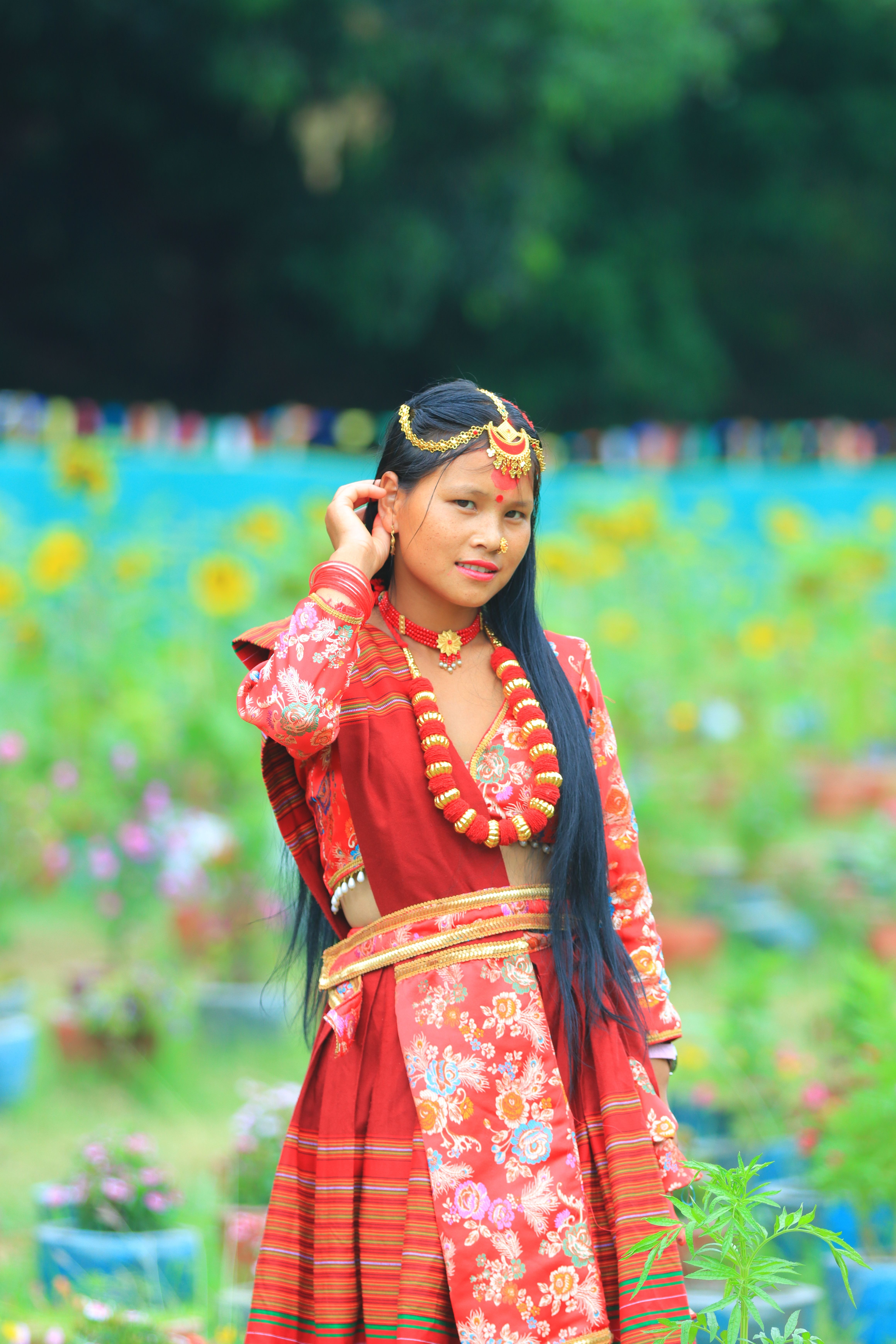 A woman in traditional attire amidst a colorful outdoor garden setting.