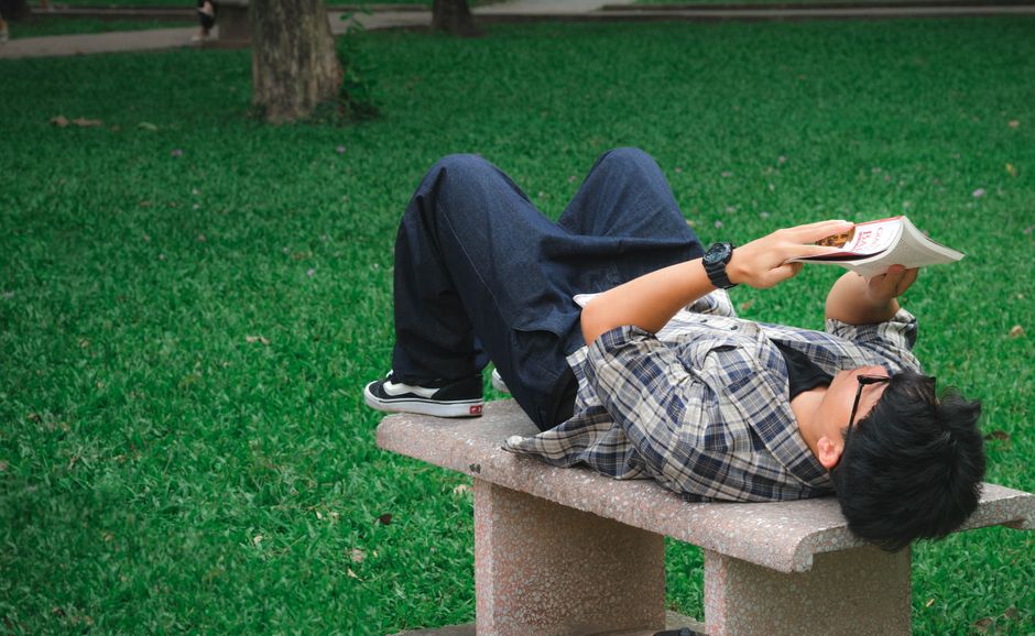 Casual young man in park lying on bench reading a book on a sunny day. Casual young man in park lying on bench reading a book on a sunny day.
